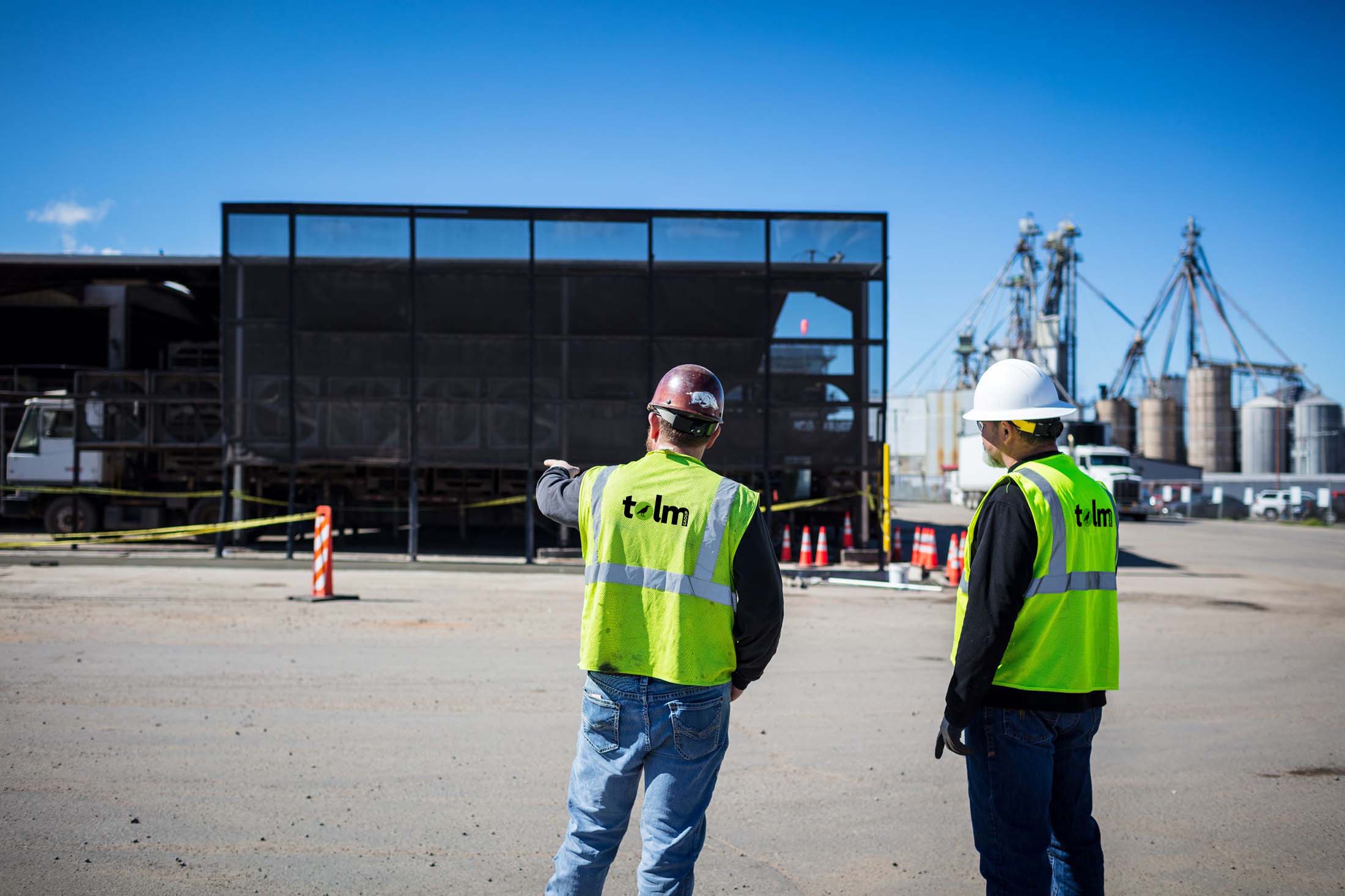 Tolm employees in construction safety gear talking in front of large structure with silos in the background